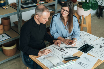 Happy Team of Furniture Designer Working Together on a New Business Projects Meeting. 
Female and male colleague sitting at table and discussing a project design using blueprints and a digital tablet.