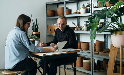 Team of Architects Working Together on a New Business Projects. 
Female and male colleague industrial designers or engineers talking about new ideas using a digital tablet and blueprints and sketches.