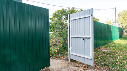Green fence. Metal fence made of profile sheet. The territory is fenced with a high fence. Ribbed surface on the street. Shooting diagonally.