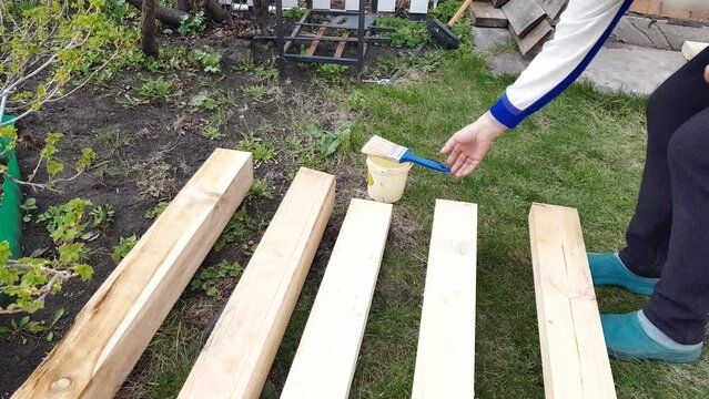 4k video, a woman's hand applies protective varnish to new lumber lying on the grass in the backyard, outdoors.