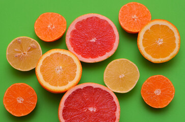 slices of different types of citrus fruits on a green background close-up