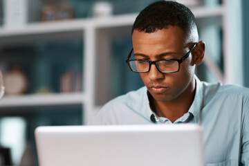 Businessmen are often very busy men. Shot of a handsome young businessman working on his laptop during a late night shift at work.