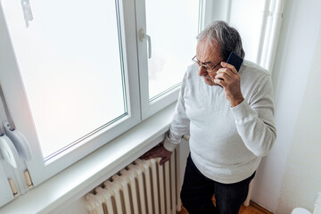 Cropped shot of an old men suffering cold at home and having problem with house heating, calling...