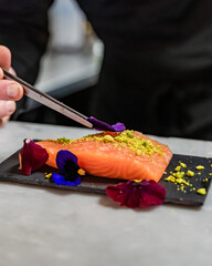 Un chef pose une pétale de fleur sur un morceau de saumon frais dans une cuisine - obrazy, fototapety, plakaty
