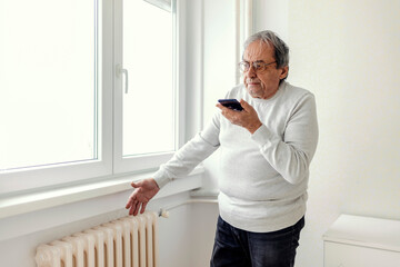 A man standing by a large window in the bedroom calls a repair service due to heating problems. An...