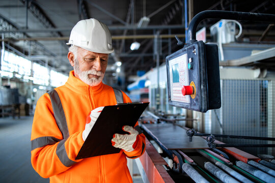 Industrial worker in safety visible uniform and hardhat inspecting process of production and machine operations in factory.
