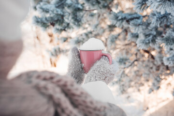 Winter image of woman's hands in the wool mittens holding vintage pink mug full of clear white snow. Winter freshness concept. Awesome snowy forest in sunny winter morning. Winter weekend out of town.