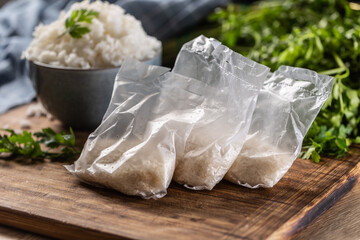 Raw rice in plastic bags on wooden background and cooked rice in bowl