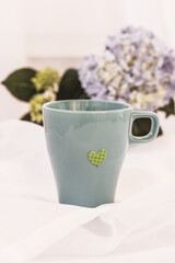 Blue mug with a heart and blue Hortensia, hydrangea flower on white background. Copy space, mock up