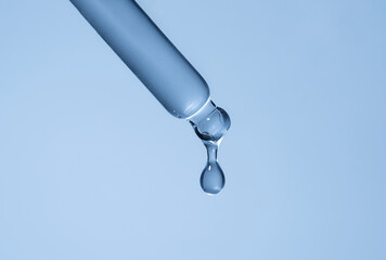 Liquid serum and dropper on a light blue background top view. Serum drops from a pipette.