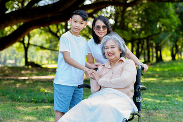 Fototapeta premium Happy senior Asian grandmother uses wheelchair with her daughter and grandchild in park, Grandson came to visit elderly grandmother and hold hand. Concept of happy family, good relationship together
