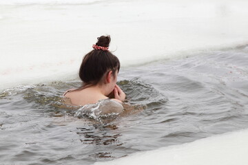 European woman swimms in icy water in an ice hole in winter.