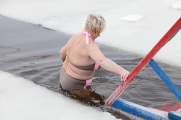 European Granny walks into the icy water to the ice hole in winter.