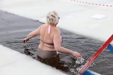 Elderly caucasian woman swimm in icy water in an ice hole in winter outdoor.
