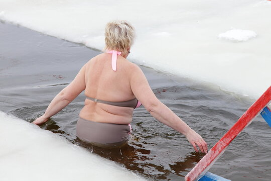 Old Russian women bathes in icy water in an ice hole in winter.