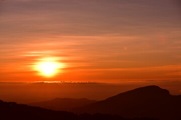 Obraz premium The sun set behind thick forests followed by mountains.
