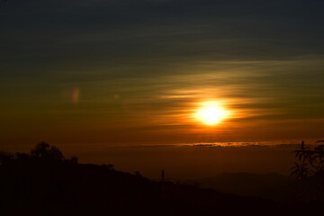 Obraz premium The sun set behind thick forests followed by mountains.