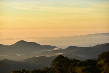 Obraz premium The sun set behind thick forests followed by mountains.