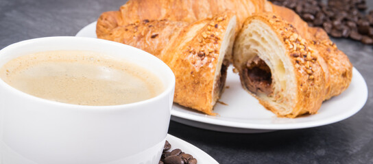 White cup of coffee and fresh croissant with chocolate for breakfast