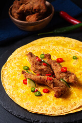 Food concept spicy Fried Chicken Tortilla Wrap with chopped chilies on black slate stone background with copy space