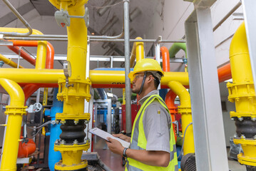 Asian engineer wearing glasses working in the boiler room,maintenance checking technical data of heating system equipment,Thailand people