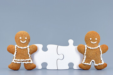 Smiling gingerbread man and woman and two connected puzzle pieces. Funny concept of partner compatibility, love or teamwork. Light blue background, copy space for text