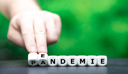Symbol for a shift from pandemic to endemic. Hand turns dice and changes the German word 