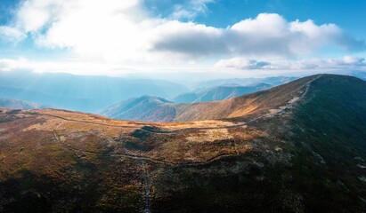 Narrow pathways on mountain ridge under blue cloudy sky