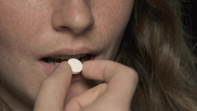 Close Up Of Young Woman Holding White Vitamins And Minerals Pill Isolated In Black Background. Healthcare And Medical Concept. Medicine For The Disease. Dieting, Eating Disorder, Weight Loss 4k