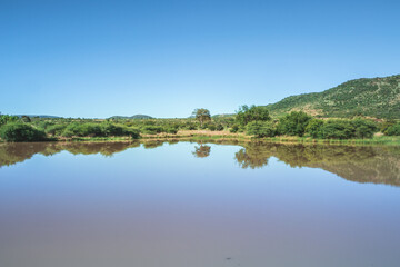 Obraz na płótnie Canvas Landscape view of a lake surrounded by mountains and green savanna grassland, Pilanesburg Nature Reserve, North West Province, South Africa