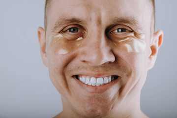 A serious man with hydrogel patches applied under his eyes looks at the camera. Individual morning skin care, anti-wrinkle, moisturizing cream, refreshing facial skin care concept 