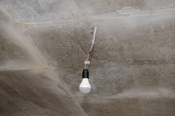 An LED light bulb hangs on a wire from a concrete ceiling