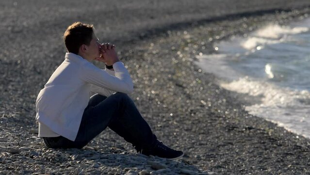 Depression and loneliness concept. Sad boy sitting on the beach thinking about school problems.