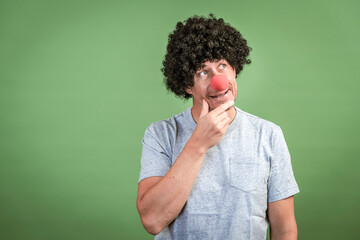 Fototapeta na wymiar Man with black wig and red clown nose posing in front of green background