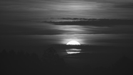 Beautiful wild sunrise and cloudy sky. The sun behind the clouds. Black and white picture