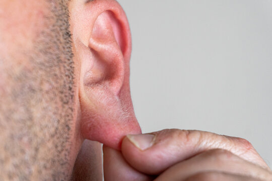 Male fingers grasp the earlobe.