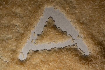 Textured rice grains, poured in one layer, form a textured surface on which the letter 