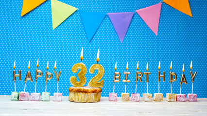 Congratulations on your birthday from the letters of the candles number 32 on a blue background with polka dots white copy space. Happy birthday muffin with burning golden candle for thirty two years 