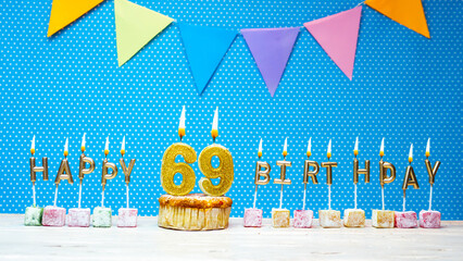 Happy birthday from number 69 candle letters on a blue background with white polka dot copy space. Happy birthday cupcake with burning golden candle for sixty nine years old
