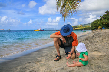 A man with a baby girl sitting at the beach at Hillsborough Bay, Carriacou Island, Grenada. - obrazy, fototapety, plakaty