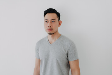 Straight face portrait of serious Asian man in grey t-shirt on white wall.