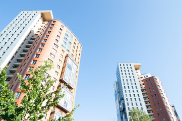 Fototapeta premium Urban city view with a tall apartment building surrounded with trees in park in summer