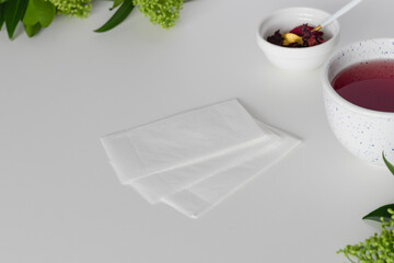 Empty tea filters, tea in a mug and dry hibiscus leaves on a white table