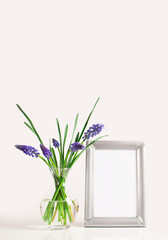Flowers bouquet in glass vase and empty photo frame on the table. Muscari, blue flowers. Mock-up for design.