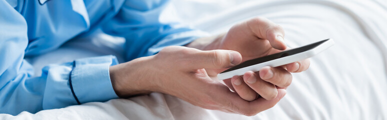 cropped view of man messaging on mobile phone in bedroom, banner.