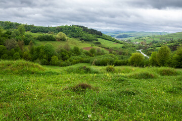 Fototapeta na wymiar carpathian countryside landscape in spring. grassy meadows, rural fields and forested slopes on hills rolling off in to the distant village in the valley. overcast weather with clouds above the ridge