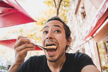 latin young man with open mouth eating a piece of cake for breakfast