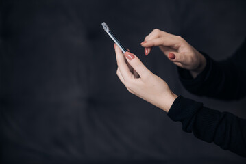 Side view of woman hand with purple polished nails holding phone overblack background with copy space.