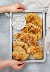 In women's hands, a baking tray with Baked cauliflower steaks with herbs and spices and mayonnaise sauce with dill, parsley and garlic. Vegan, vegetarian cuisine. Selective focus, top view