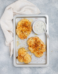 Baked cauliflower steaks with herbs and spices on a baking sheet on a gray concrete background. Mayonnaise sauce with dill, parsley and garlic. Vegan, vegetarian cuisine. Selective focus, top view